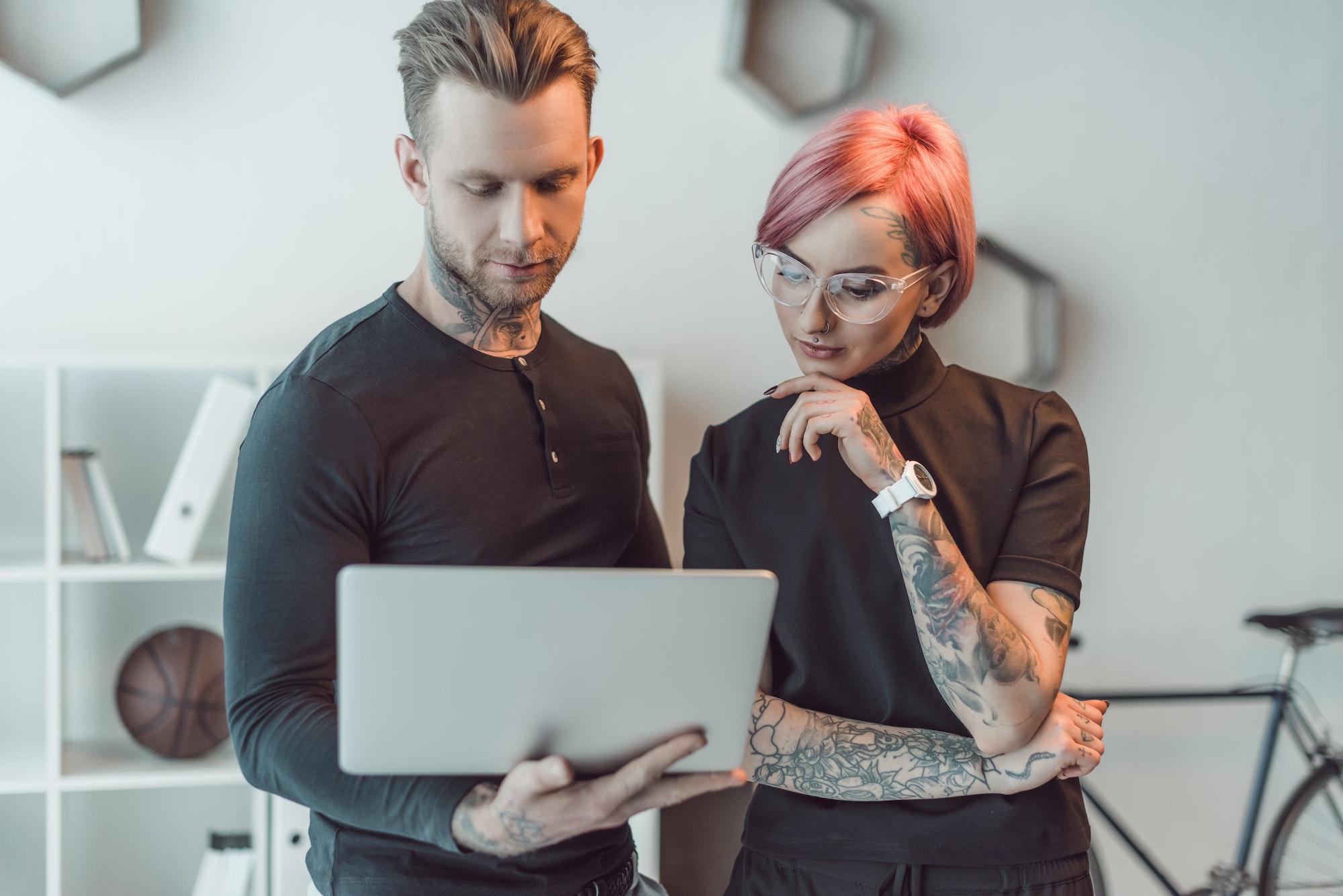 young tattooed colleagues using laptop together in office